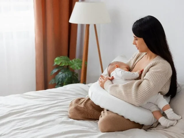 a mother sitting on the bed while holding her sleeping baby