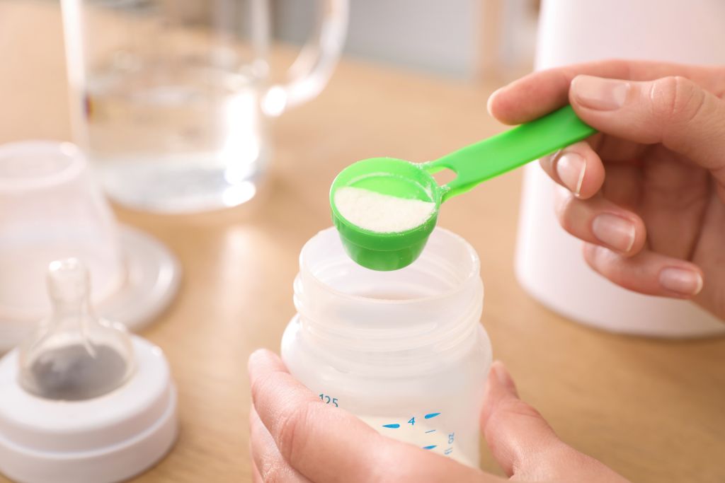 Confinement nanny in Singapore preparing infant milk formula, carefully measuring baby formula powder as part of professional newborn feeding and postnatal care