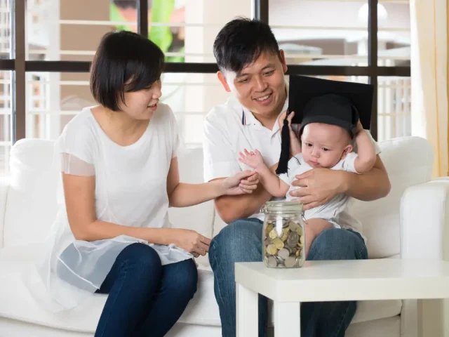 Parents holding their newborn child with a toga hat on his head. A nanny in Singapore can help build confidence with parents to look after their child on their own.