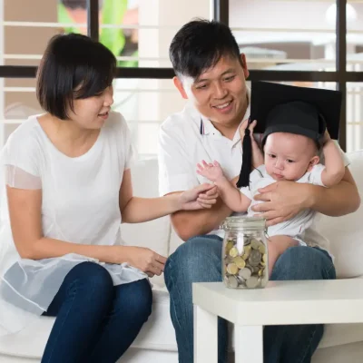 Parents holding their newborn child with a toga hat on his head. A nanny in Singapore can help build confidence with parents to look after their child on their own.