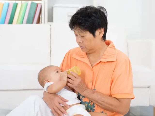 An elderly confinement nanny in Singapore bottle-feeding an infant