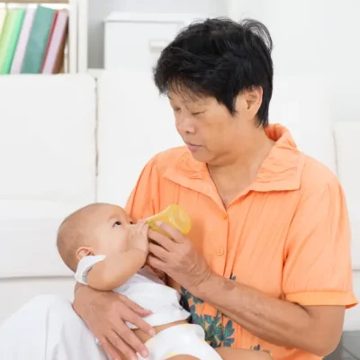 An elderly confinement nanny in Singapore bottle-feeding an infant